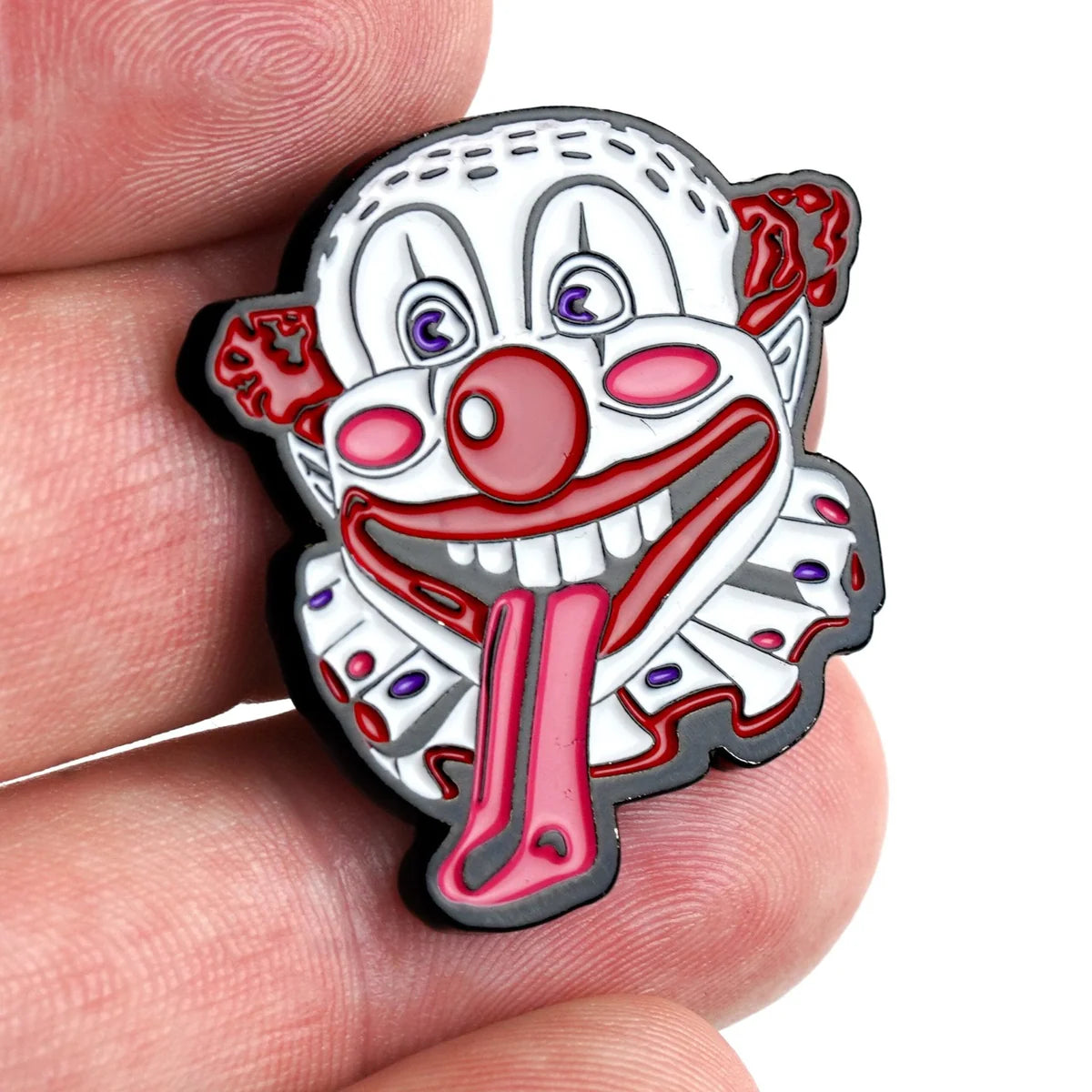 A close-up of the Bogey Bros "Happy Land Clown" enamel pin held between fingers, with a wide open mouth, long red tongue, red nose, and bold features—this could be Happy's nemesis in pin form.