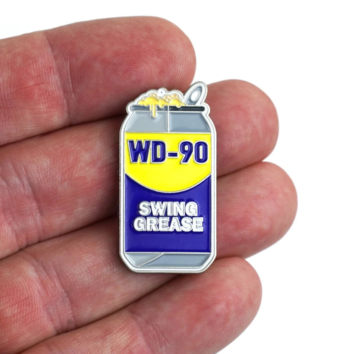 A hand holds Bogey Bros’ Swing Grease enamel pin, shaped like a can with yellow liquid dripping—this playful parody of the classic WD-40 is perfect for golfers wanting a fun accessory to fix their swing.
