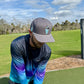 A man in a Logie Joe's Golf Astronaut Walker Golf Hat—Snapback Cap with built-in magnetic ball marker holder—is preparing to hit a golf ball on a green course under a partly cloudy sky.