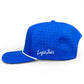 The Water Ball Golf Hat by Logie Joe's Golf is a bright blue adjustable snapback cap with a built-in magnetic ball marker holder (marker included) and white embroidered Logie Joe's text on the side. Background: plain white.
