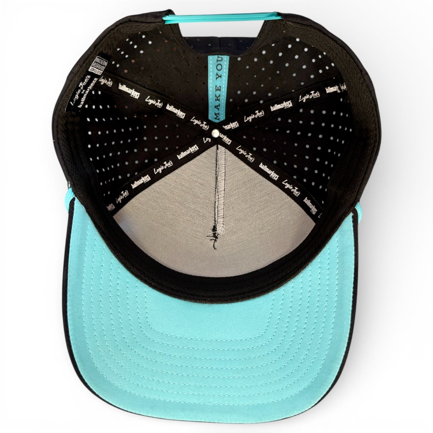 Top-down view of the turquoise Logie Joe’s Golf Shark Bite Snapback Cap, featuring a black band, polka dot lining, stitched brim, and labels. This adjustable hat includes a built-in magnetic ball marker holder with marker.