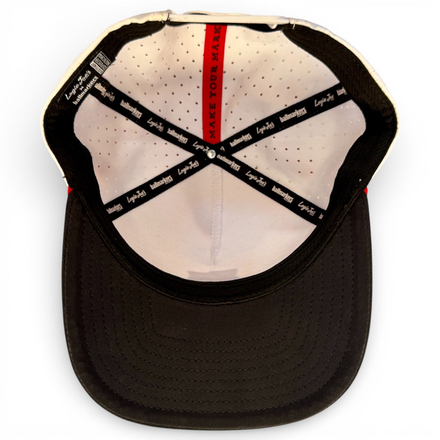 The inside of the Logie Joe's Golf Pocket Aces gray and black snapback cap features black sweatbands with white logos, perforated white lining, a red "MAKE YOUR MARK" strip, and a built-in magnetic ball marker holder with marker included.