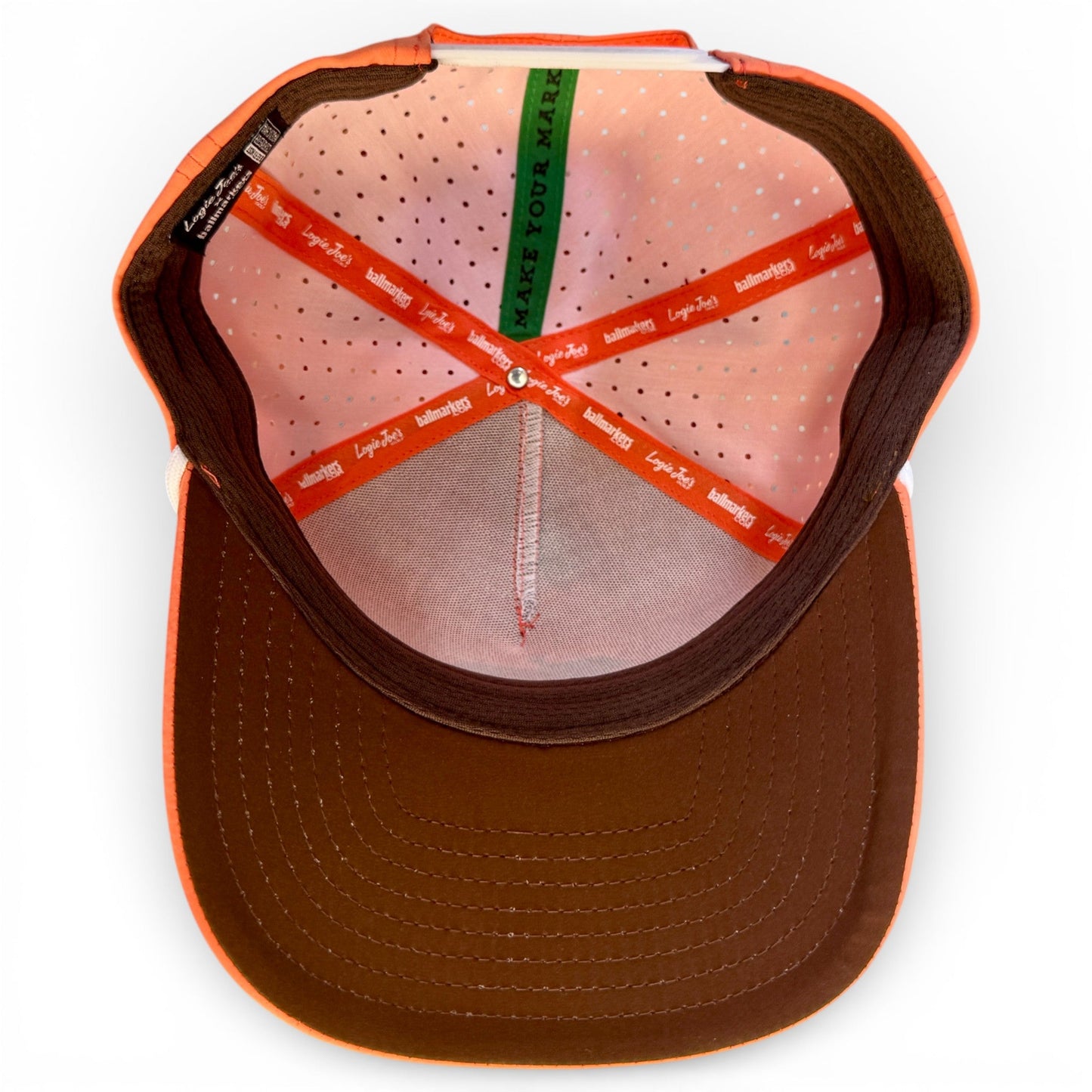 The Just Peachy Golf Hat by Logie Joe's Golf is a peach snapback cap with a perforated lining, colorful bands, and a green MAKE YOUR MARK band. It features an adjustable fit plus a built-in magnetic ball marker holder and included marker.