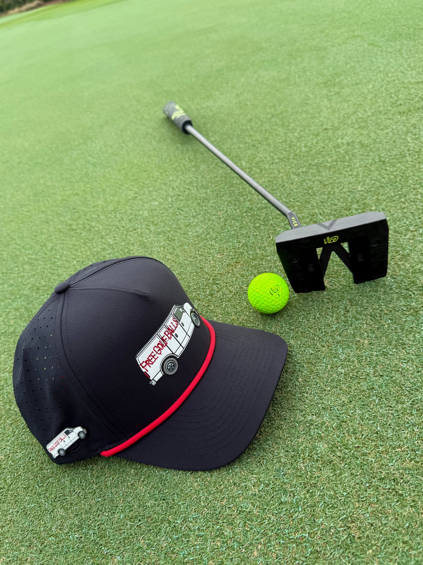 The Logie Joe's Golf Free Golf Balls Van Snapback Hat with matching neon green ball marker sits beside a black putter on green turf.