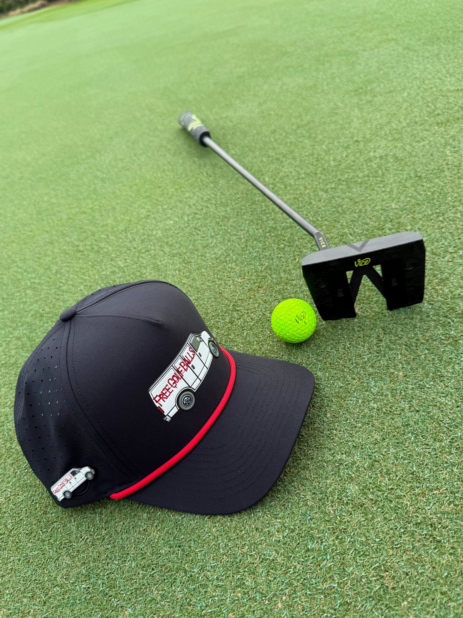 The Logie Joe's Golf Free Golf Balls Van Snapback Hat with matching neon green ball marker sits beside a black putter on green turf.