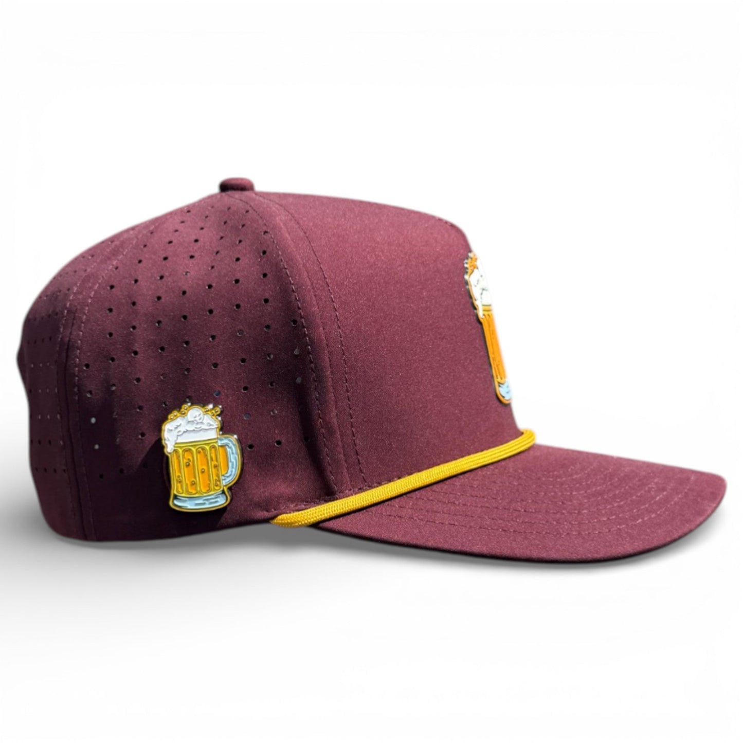 The Logie Joe's Golf Cold One Golf Hat is a maroon adjustable snapback with yellow trim, featuring two beer mug enamel pins and ventilation holes. It includes a built-in magnetic ball marker holder, comes with a marker, and is shown on a white background.