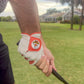 A person wearing the Breakfast Ball Cabretta Leather Golf Glove by Logie Joe’s Golf, a premium glove featuring a magnetic ball marker, grips a golf club on a grassy course with houses and palm trees in the background.