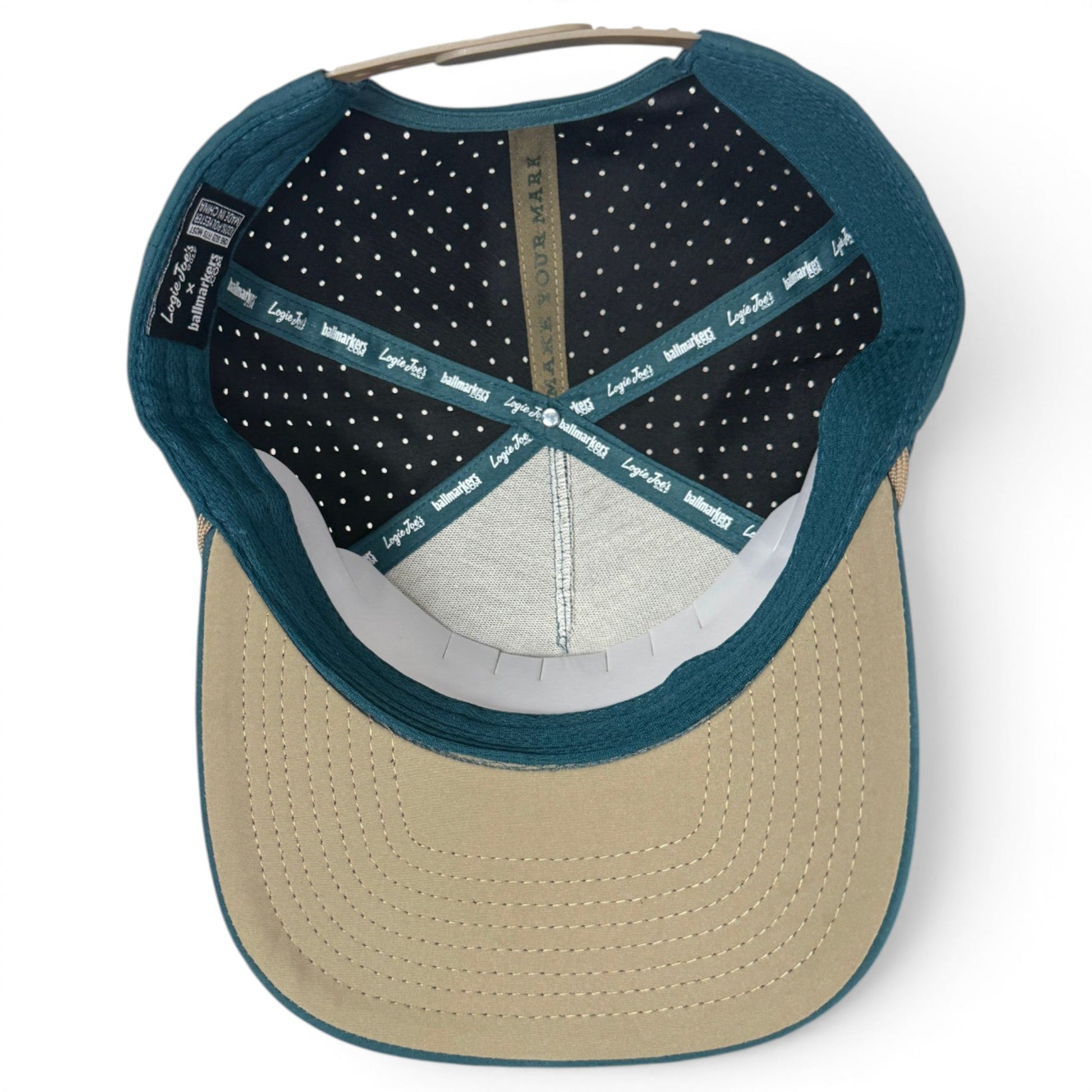 Here’s a revised version of the sentence using the supplied product data: A look inside the Logie Joe’s Golf Deep Dive Golf Hat reveals a beige brim, blue edge, black interior with white dots, and branded tape crossing the crown. This adjustable snapback cap features a built-in magnetic ball marker holder (plus marker included), ensuring both comfort and convenience on the course.