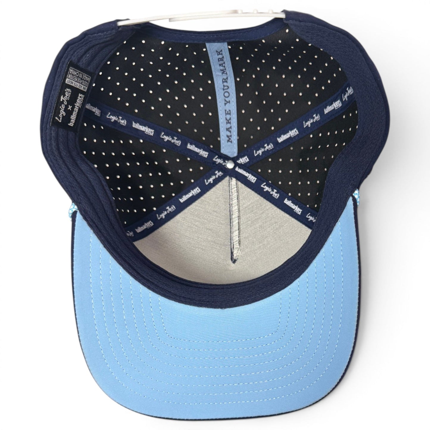 Blue Zero Chill Yeti Golf Hat by Logie Joe’s Golf shown from above, revealing the interior. This breathable snapback cap features a black lining with white polka dots, navy blue trim labeled “Loyal to Few,” and a light blue brim. The inner band displays the words “MAKE YOUR MARK.” Inspired by performance-driven designs, this adjustable hat also includes a built-in magnetic ball marker holder with marker included—perfect for convenience on the course.
