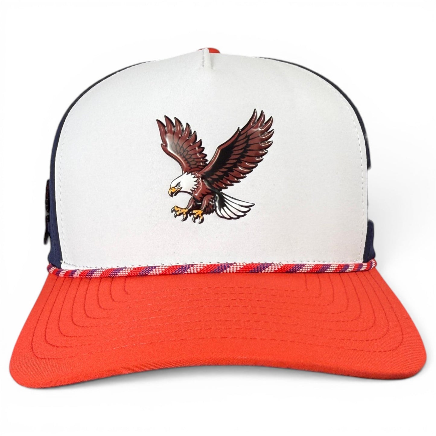 Introducing the Freedom Flight Golf Hat by Logie Joe’s Golf, an adjustable snapback cap featuring a bold graphic of a flying bald eagle on the white and red front panel, finished with a red, white, and blue braided rope detail above the red brim. With classic American style, this hat also includes a built-in magnetic ball marker holder and marker for ultimate convenience on the course.