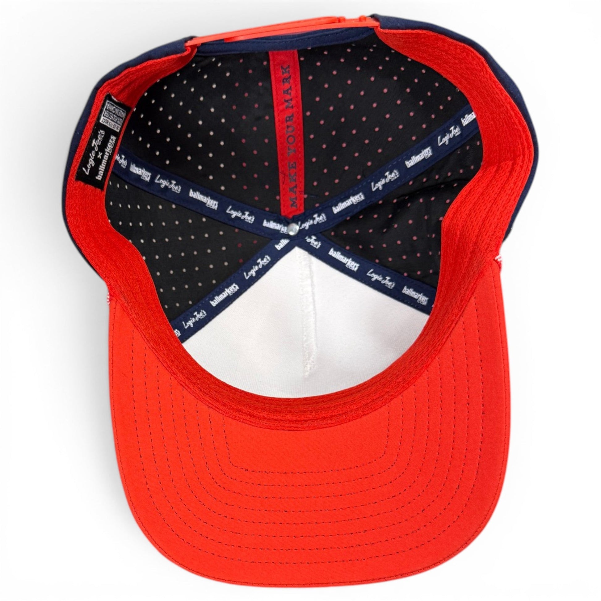 A top-down view of the inside of the Logie Joe’s Golf Freedom Flight Golf Hat—a red, white, and blue snapback cap—showing the tags, polka dot lining, and the phrase MAKE YOUR MARK on the inner band. This premium golf hat features thoughtful American-inspired details like a built-in magnetic ball marker holder with a marker included.