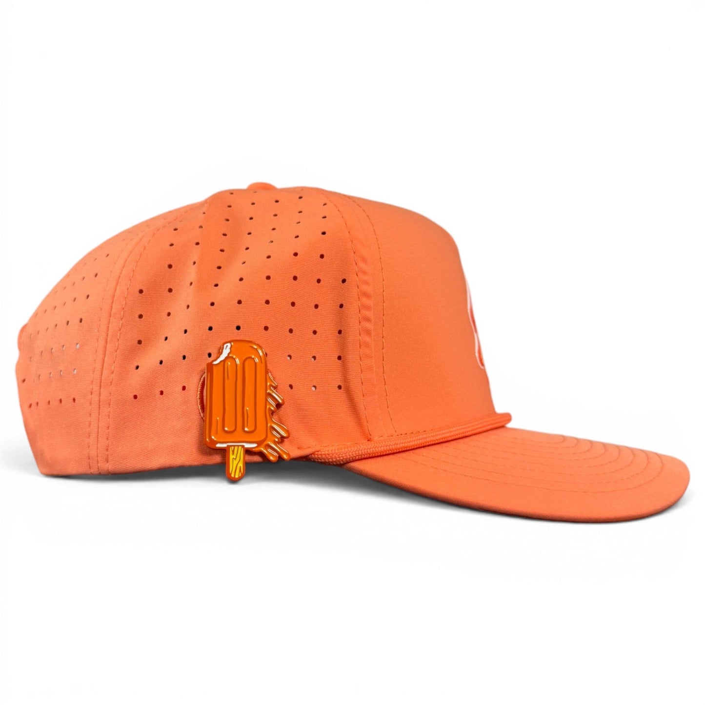 Introducing the Orange Dream Golf Hat by Logie Joe’s Golf—a snapback cap featuring small ventilation holes for breathability and an adjustable fit. This hat includes a built-in magnetic ball marker holder on the side, complemented by an included orange popsicle-shaped marker.