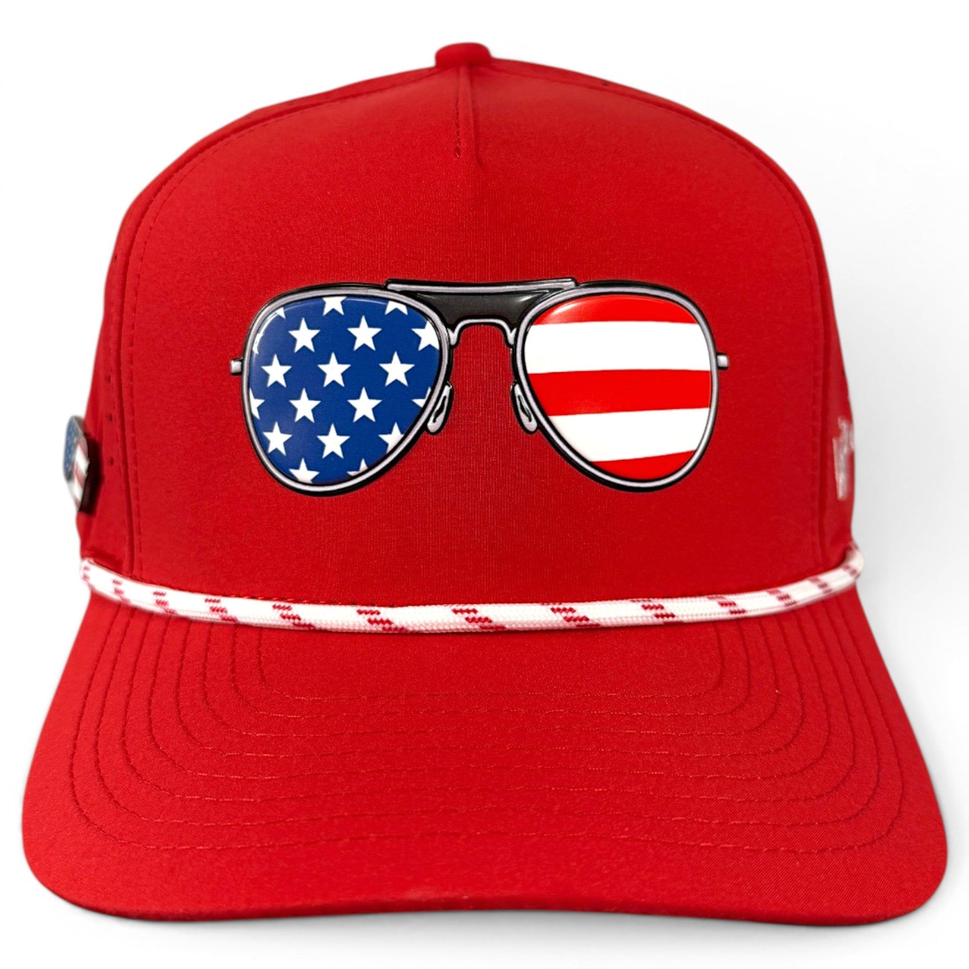 Introducing the Red, White & View Golf Hat by Logie Joe’s Golf—a stylish red snapback cap featuring sunglasses adorned with USA flag designs: one lens covered in white stars on blue and the other in bold red and white stripes, capturing patriotic flair. This adjustable cap comes equipped with a built-in magnetic ball marker holder and an included marker, making it the perfect blend of patriotic style and golf-ready functionality.