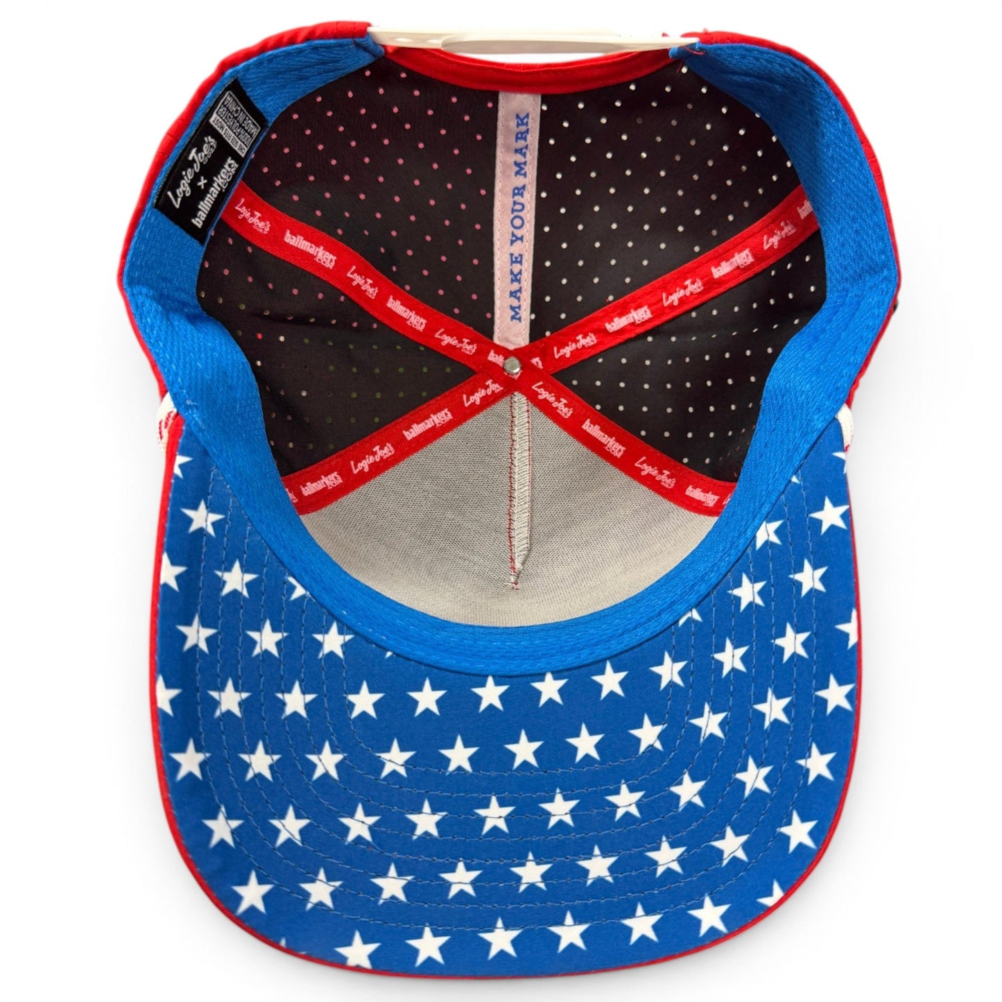 The inside of the Red, White & View Golf Hat by Logie Joe’s Golf features a blue snapback cap with white stars on the brim, red accents, and “MAKE YOUR MARK” printed on the inside headband.