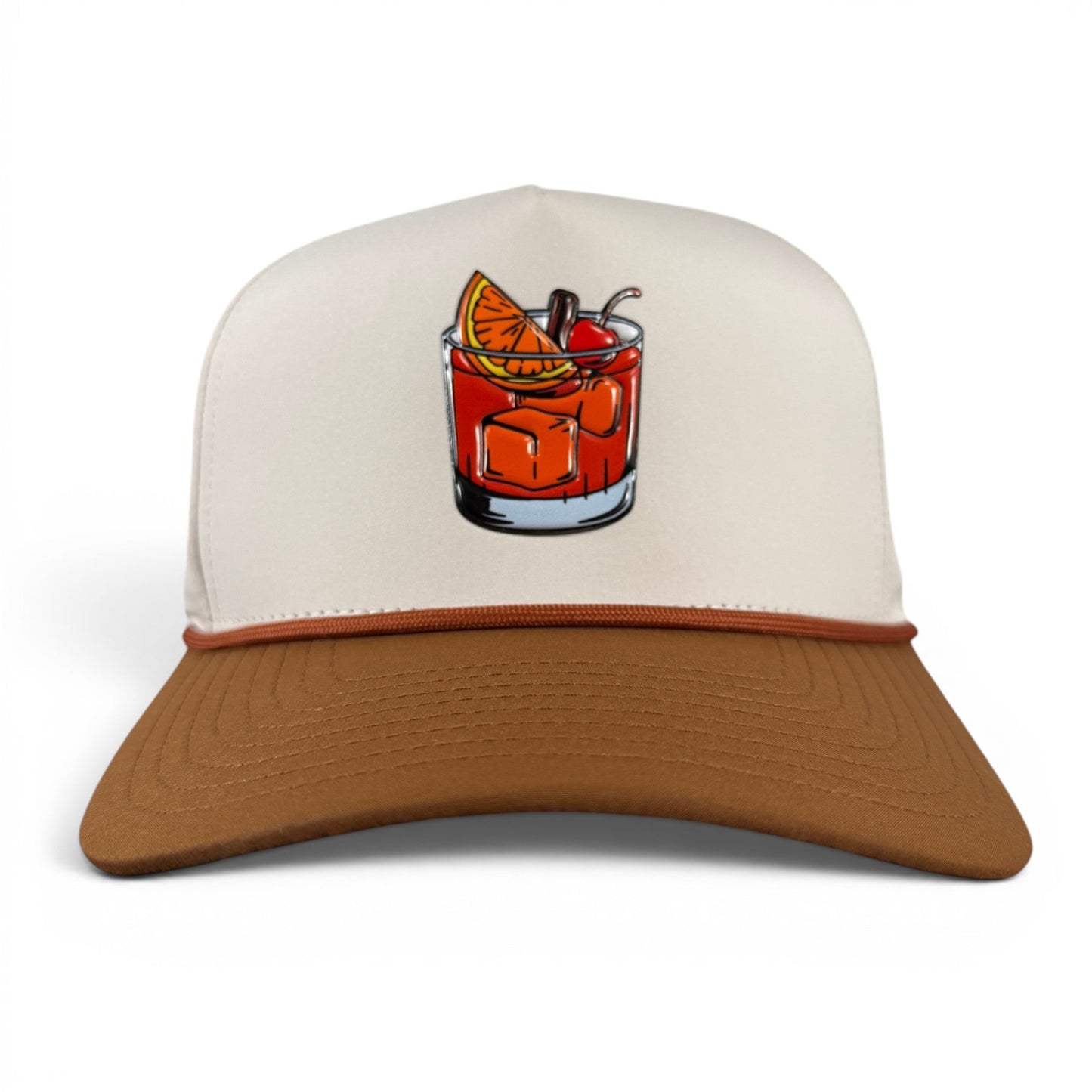 Introducing the Old Fashioned Golf Hat by Logie Joe’s Golf—a snapback cap featuring a crisp white crown and brown brim, accented with an illustration of a cocktail with ice, an orange slice, and a cherry on the front. Designed for golf enthusiasts, this adjustable hat comes complete with a built-in magnetic ball marker holder and includes a marker, ensuring you’re always ready on the green.