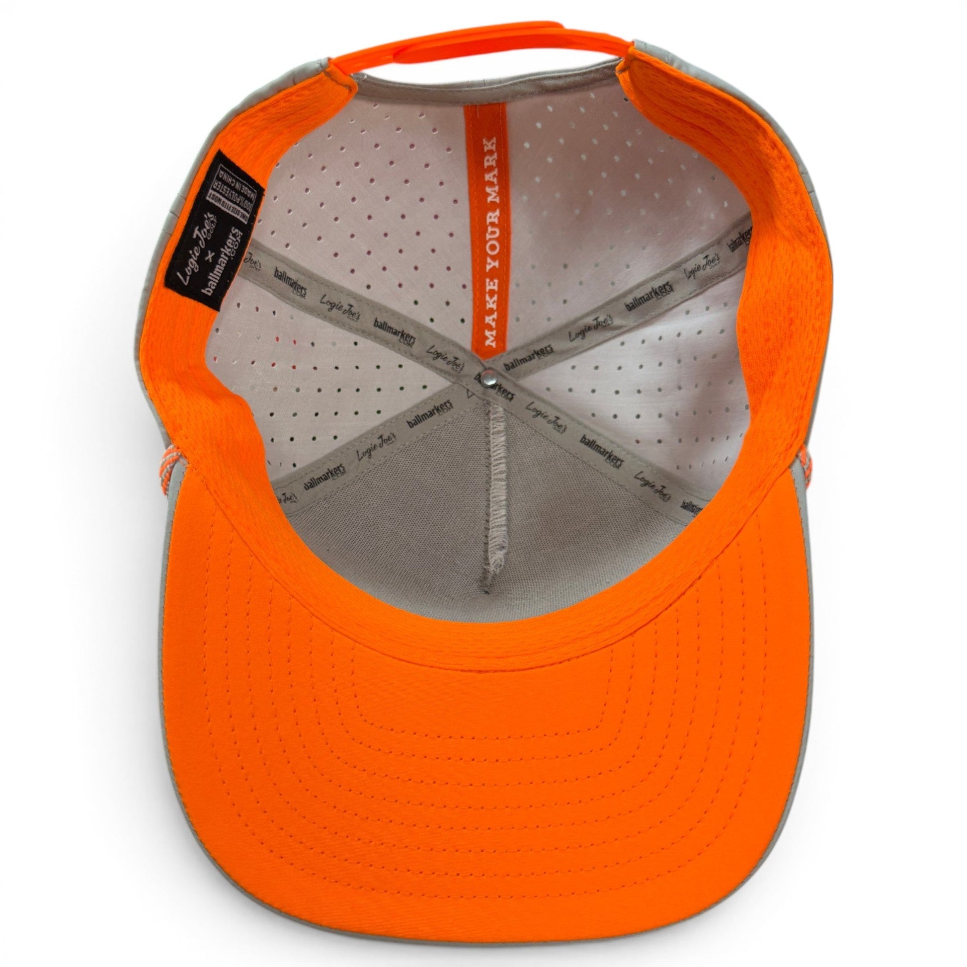 Here’s your revised sentence using the provided product data: Inside view of an orange Logie Joe’s Golf Fossil Fairway Golf Hat | Snapback Cap, showing the grey interior with ventilation holes, crisscrossed seams, a tag, and the phrase MAKE YOUR MARK printed under the front panel. This adjustable cap also features a built-in magnetic ball marker holder with marker included for added convenience on the course.