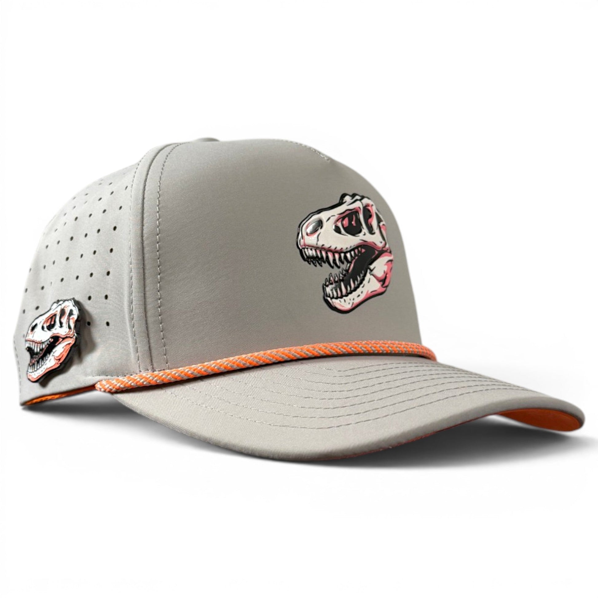 A light gray snapback cap from Logie Joe’s Golf, the Fossil Fairway Golf Hat features bold orange trim and showcases a dinosaur skull graphic on the front panel with a smaller matching detail on the side. Designed for golfers, this adjustable hat includes small ventilation holes for added comfort, plus a built-in magnetic ball marker holder and marker.