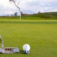A close-up of an OnPointGolf.us One Rail Smooth Ball Marker used as a putting aid with a golf putter and ball on green grass; a flag and trees appear blurred in the background.
