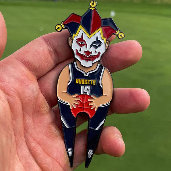 A hand holds the Pin Creatures Joker—a novelty golf divot tool shaped like a jester in a Denver Nuggets jersey, featuring a clown face and red basketball. Add playful style to your game and pair it with your favorite ball marker or hat clip.