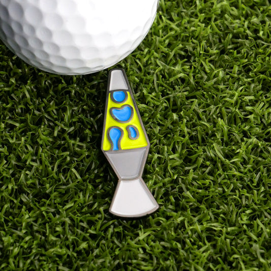 A white golf ball sits on green grass next to the Ballmarkers.com Lava Lamp Ball Marker, featuring bright blue and yellow details—a playful reminder to stay in the flow on the course.