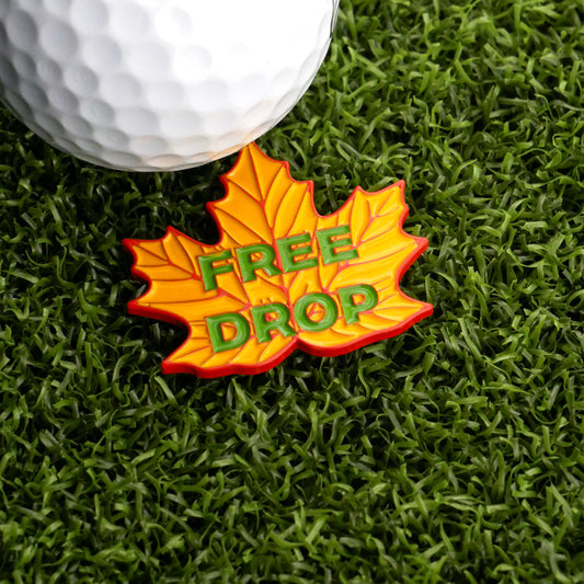 The Ballmarkers.com Free Drop Leaf Ball Marker, shaped like a yellow and orange maple leaf with "FREE DROP" in green, adds a unique touch to your game—ideal for golfers seeking distinctive markers.