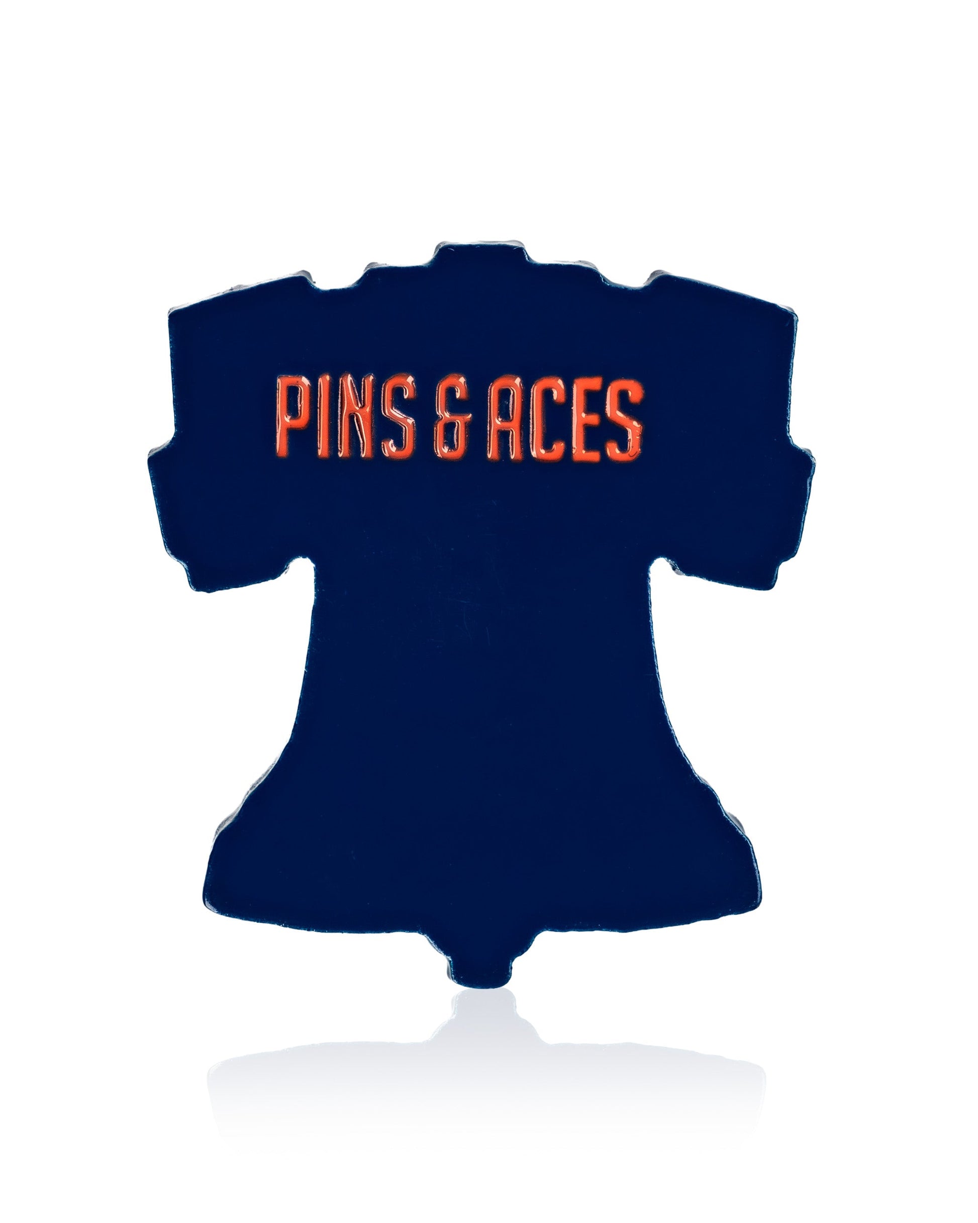 The Liberty Bell - Ball Marker by Pins and Aces is a navy blue, bell-shaped golf accessory featuring "PINS & ACES" in bold orange letters on a white background—perfect for any golf enthusiast.