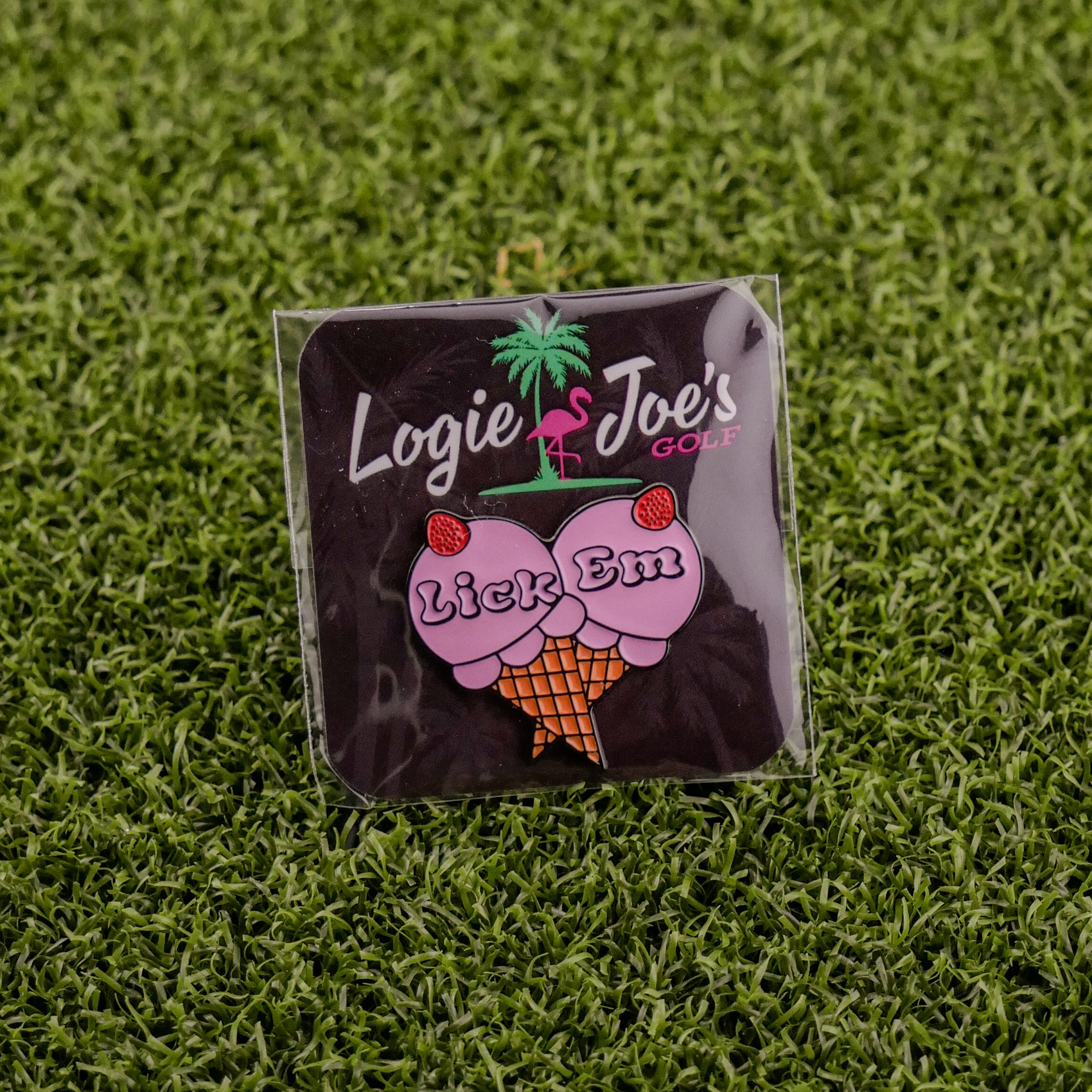 Add a playful touch to your game with Ballmarkers by Logie Joes Lick Em golf ball marker, featuring an ice cream cone with cherry-topped scoops and the phrase “Lick Em.” Displayed on artificial grass for a fun twist.