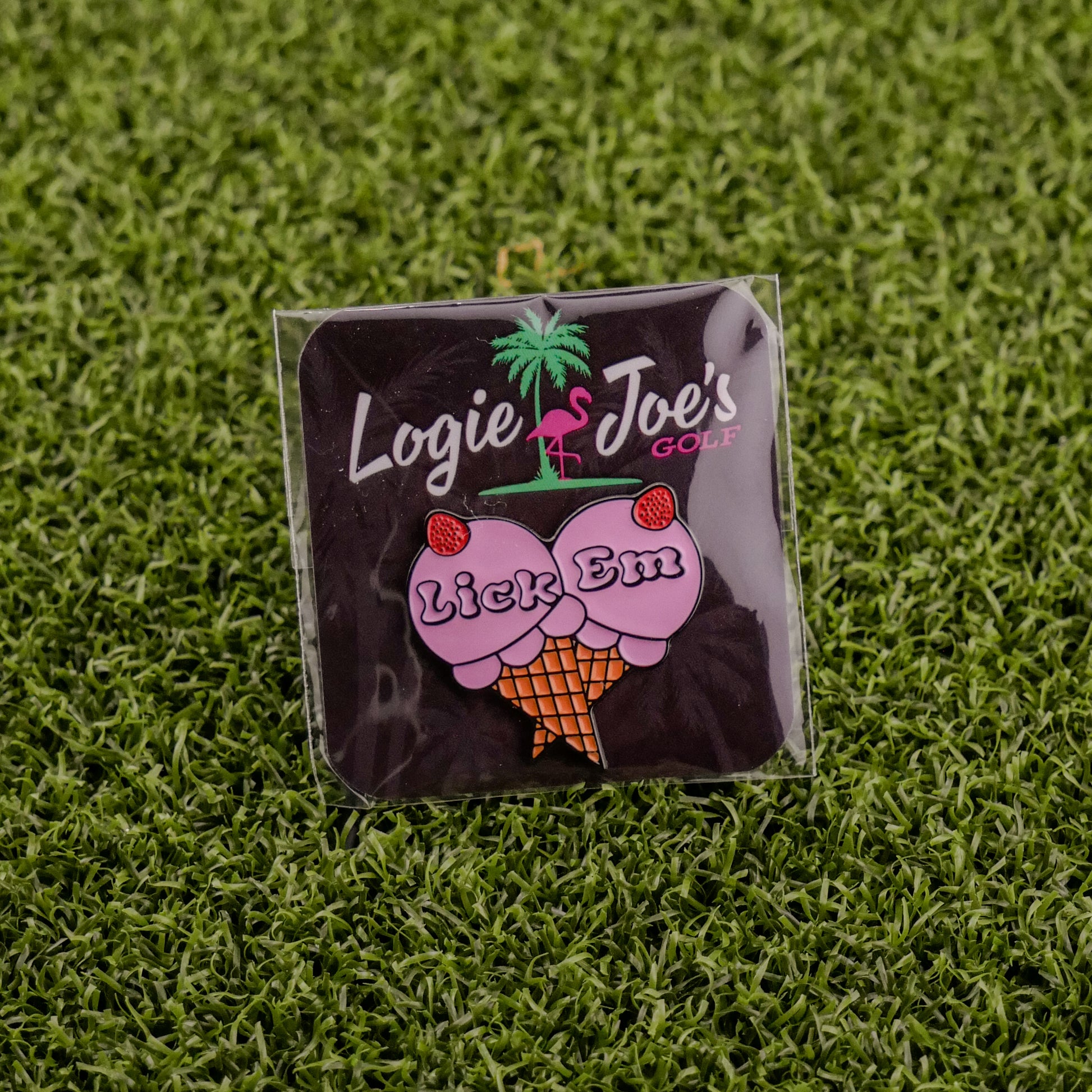 Add a playful touch to your game with Ballmarkers by Logie Joes Lick Em golf ball marker, featuring an ice cream cone with cherry-topped scoops and the phrase “Lick Em.” Displayed on artificial grass for a fun twist.