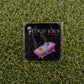 A square sticker on green artificial grass features “LOGIE JOE'S GOLF” above a bathtub and rubber duck, with “Live Laugh Toaster Bath,” adding playful charm to your premium golf accessories or golf ball markers.