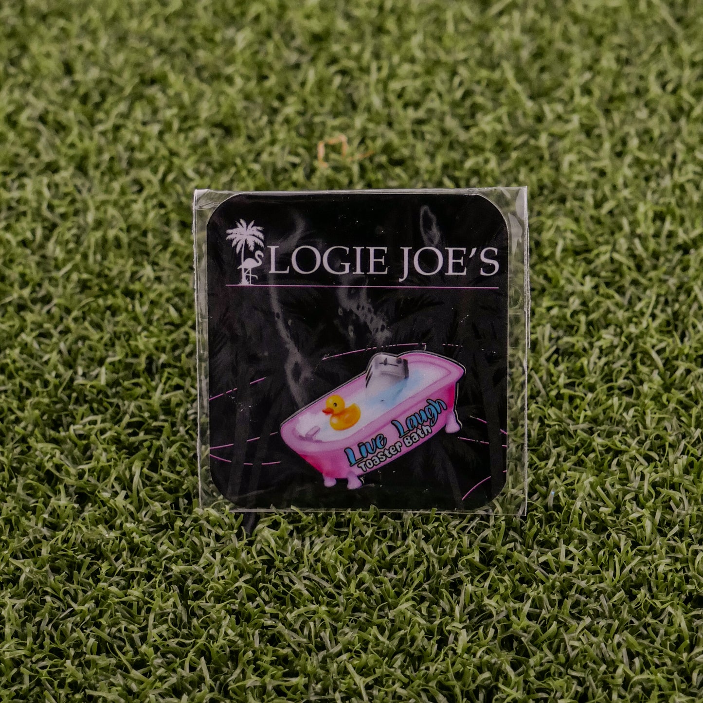 A square sticker on green artificial grass features “LOGIE JOE'S GOLF” above a bathtub and rubber duck, with “Live Laugh Toaster Bath,” adding playful charm to your premium golf accessories or golf ball markers.