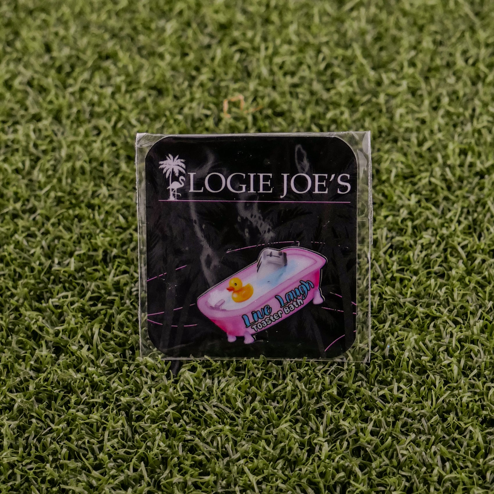 A square sticker on green artificial grass features “LOGIE JOE'S GOLF” above a bathtub and rubber duck, with “Live Laugh Toaster Bath,” adding playful charm to your premium golf accessories or golf ball markers.
