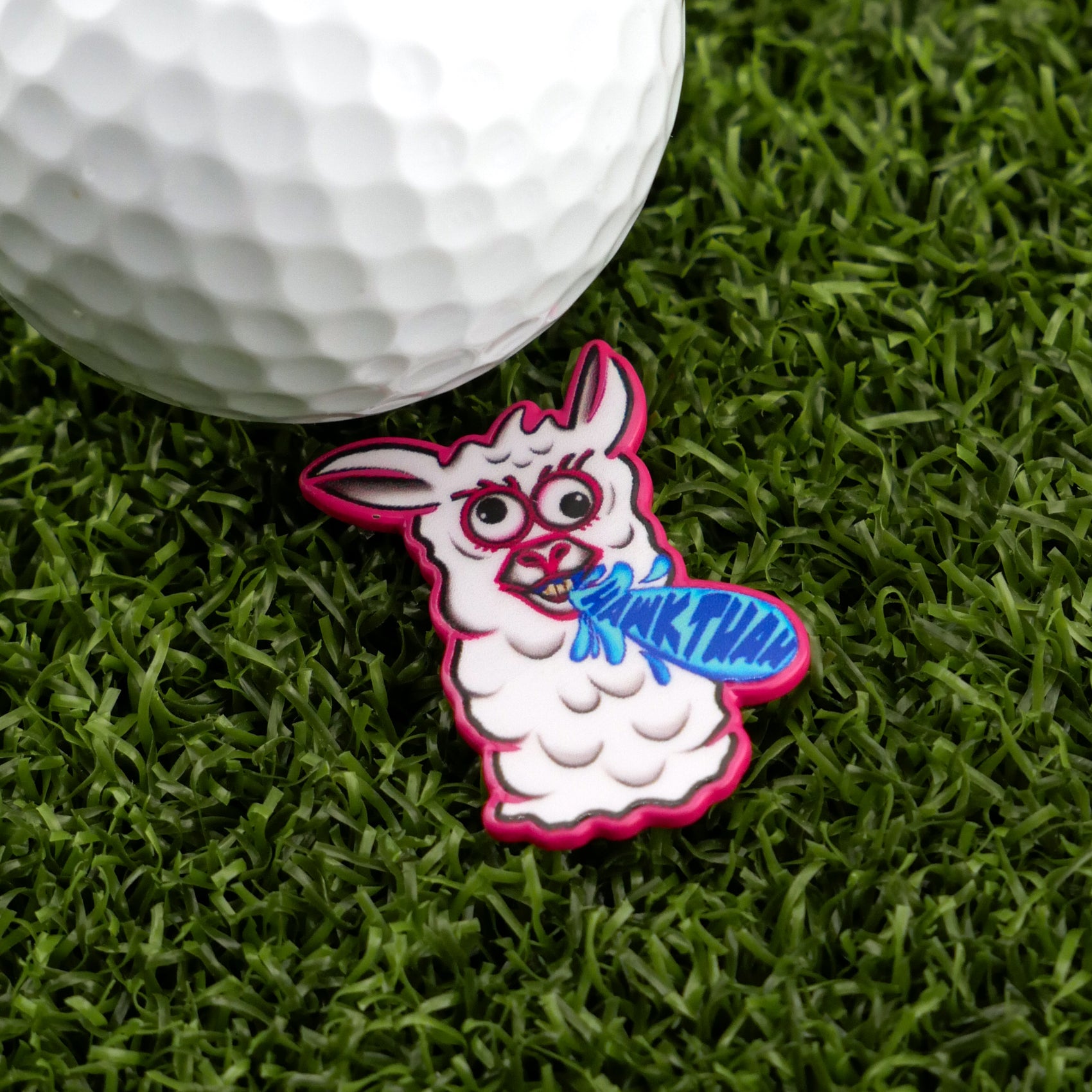 The Hawk Tuah Llama by Logie Joe's Golf is a cartoon llama-shaped ball marker with a blue "THANK LHAM!" speech bubble, seen next to a white golf ball—a fun, premium accessory for any golfer's collection.