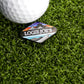 A golf ball on artificial grass sits next to the Logie Joe's Golf Ball Marker, featuring the Logie Joe's Golf mountain wave logo and colorful landscape artwork.