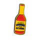 The Louisiana Hot Sauce Ball Marker from Pins and Aces is a pin shaped like a hot sauce bottle, featuring a yellow and red label with "The Original Louisiana Brand Hot Sauce" on a white background.