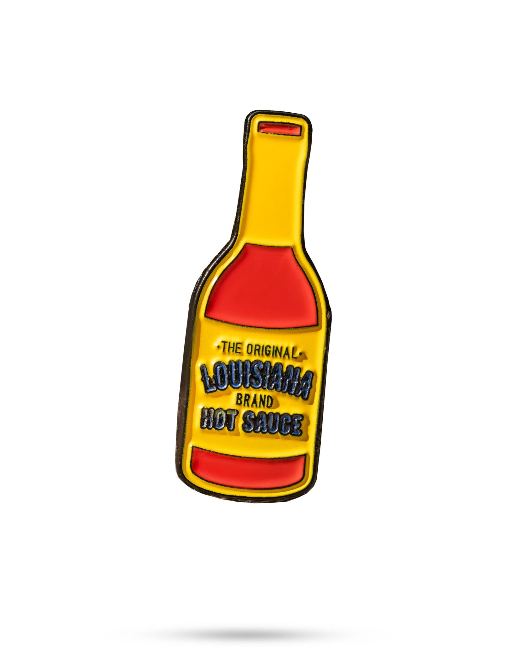 The Louisiana Hot Sauce Ball Marker from Pins and Aces is a pin shaped like a hot sauce bottle, featuring a yellow and red label with "The Original Louisiana Brand Hot Sauce" on a white background.