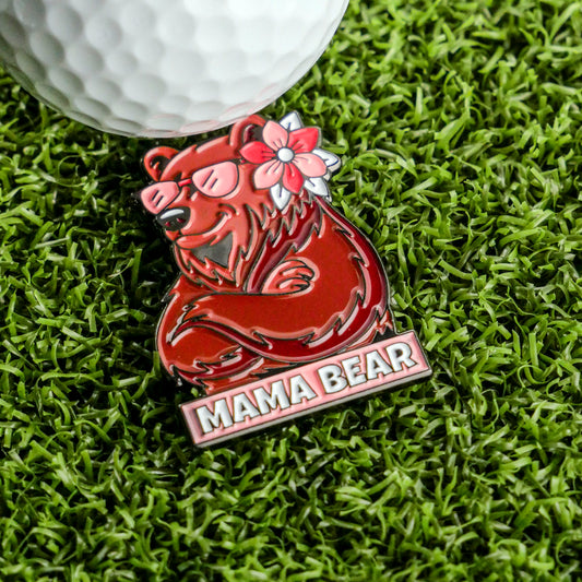 The Mama Bear Ball Marker by Ballmarkers.com, featuring a red design with a flower and sunglasses, sits on green artificial grass beside a white golf ball—an ideal ladies' golf accessory or Mother’s Day gift.