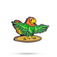 The Margaritaville - Surfing Parrot Ball Marker by Pins and Aces features a vibrant cartoon parrot with green wings, an orange head, and a yellow beak standing on a surfboard—great for golf accessory fans.