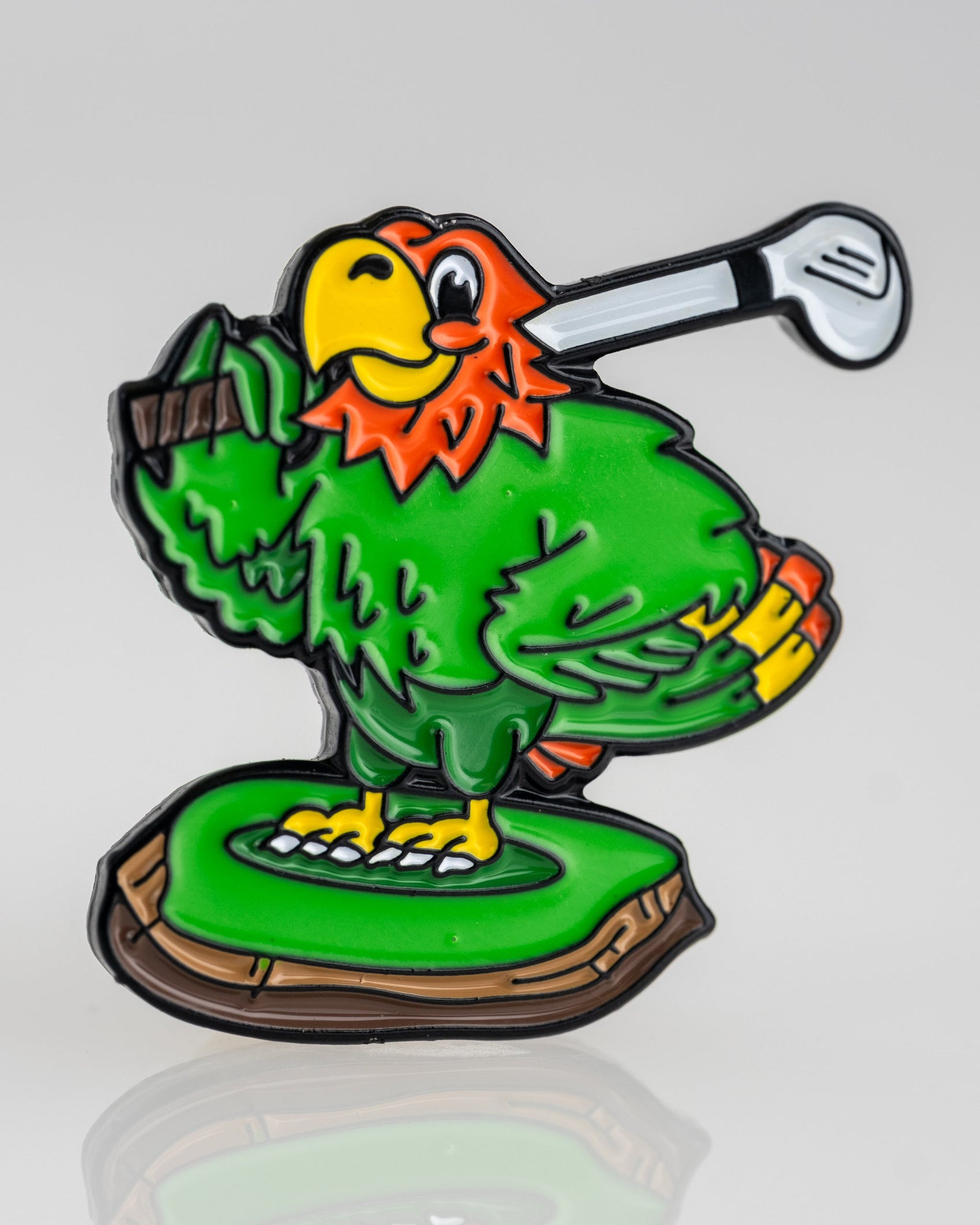 A colorful cartoon parrot with green feathers and an orange head stands on grass, holding a golf club and smiling—featured on the Margaritaville - Golfing Parrot Ball Marker by Pins and Aces.