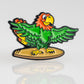 A colorful cartoon parrot with red, green, and yellow feathers stands on a yellow surfboard, wings spread wide. Inspired by Pins and Aces, this Margaritaville - Surfing Parrot Ball Marker is shown against a plain white background.
