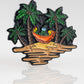 The Margaritaville - Sleeping Parrot Ball Marker by Pins and Aces features a vibrant design of a parrot napping in a hammock between palm trees on a tropical island, adding color and fun to your golf gear.