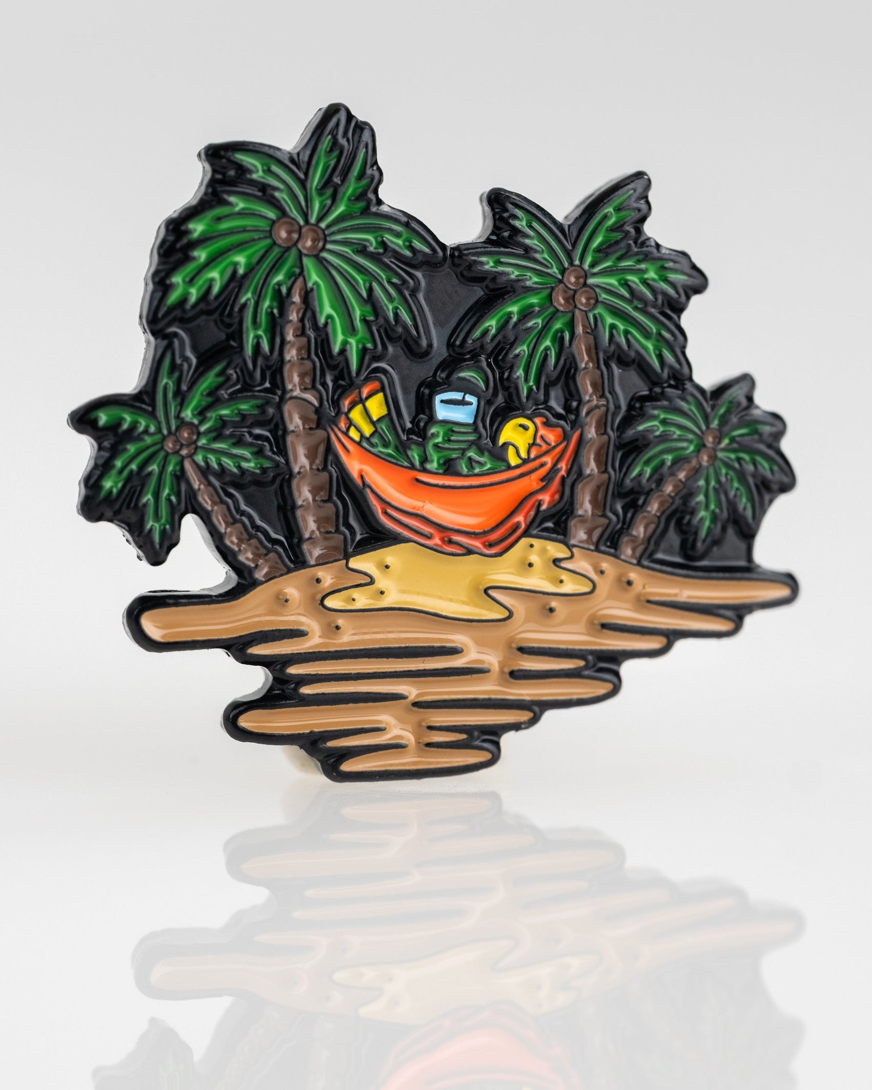 The Margaritaville - Sleeping Parrot Ball Marker by Pins and Aces features a vibrant design of a parrot napping in a hammock between palm trees on a tropical island, adding color and fun to your golf gear.