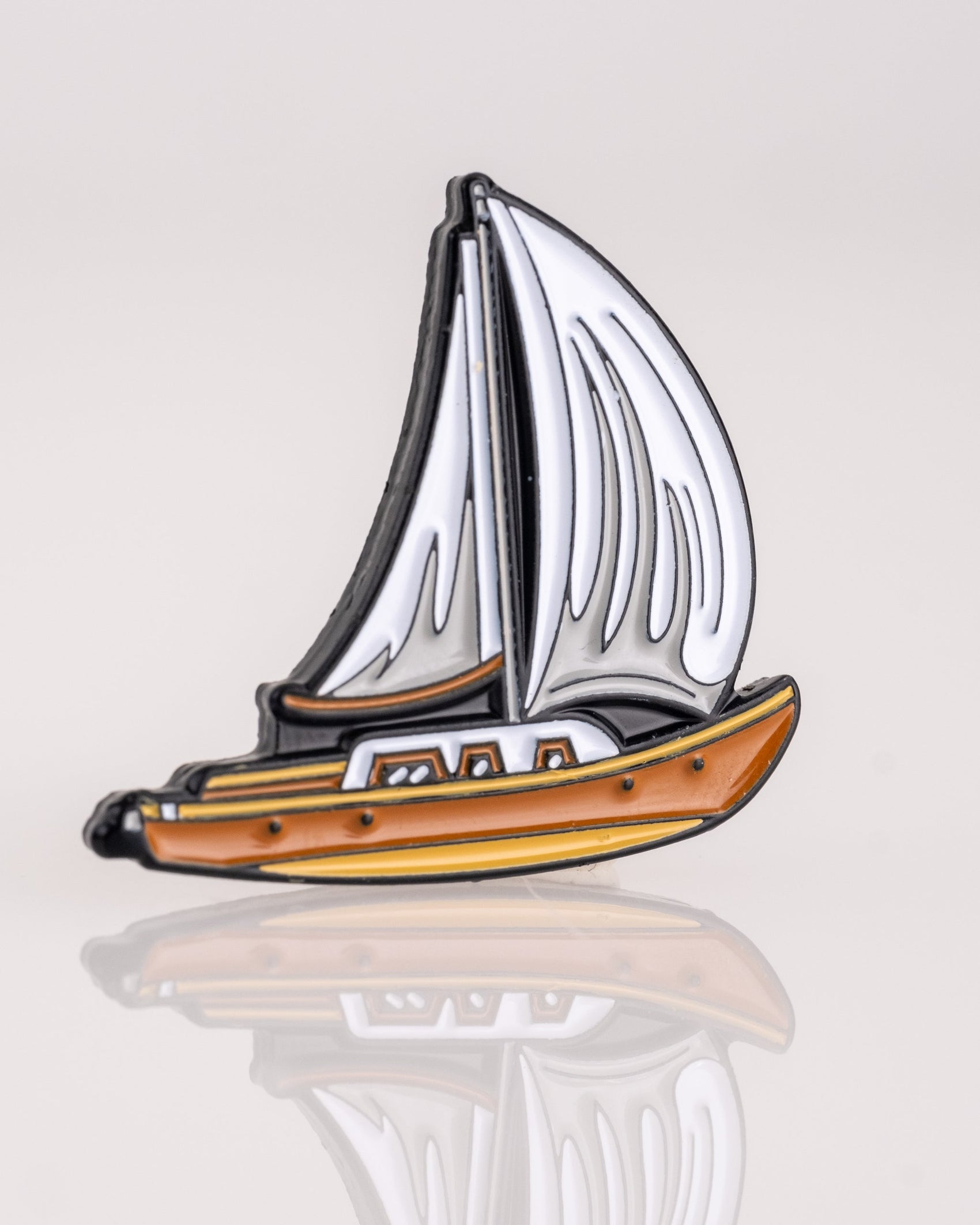 The Margaritaville - Sailboat Ball Marker by Pins and Aces is a small enamel pin with a brown hull and white sails—ideal as a golf ball marker or as part of the exclusive Pins and Aces Margaritaville collection.