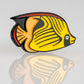 A vibrant Angel Fish with yellow, black, and orange markings appears on a light gray background with a polished reflection—featured in the Margaritaville - Angel Fish Ball Marker by Pins and Aces.