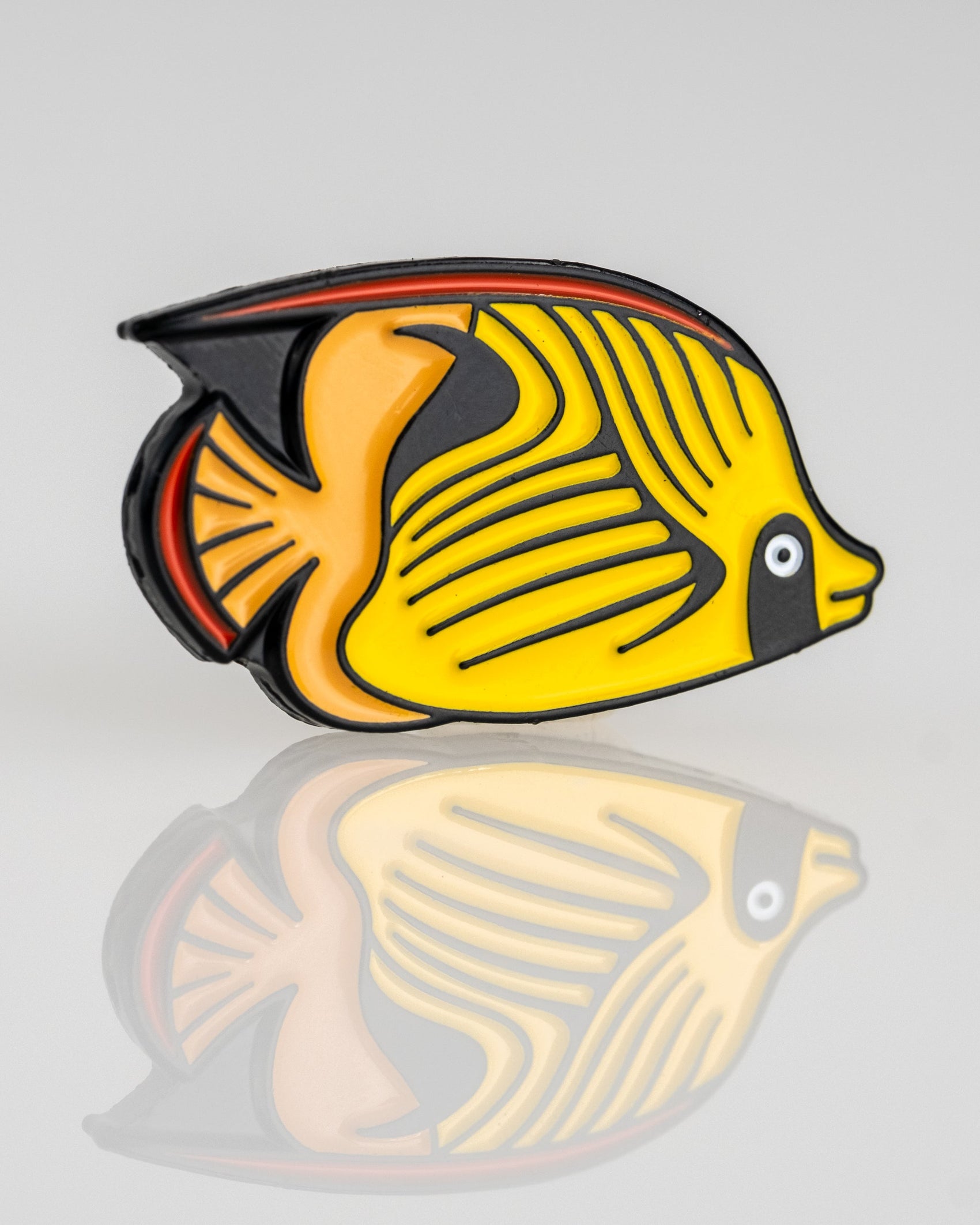 A vibrant Angel Fish with yellow, black, and orange markings appears on a light gray background with a polished reflection—featured in the Margaritaville - Angel Fish Ball Marker by Pins and Aces.