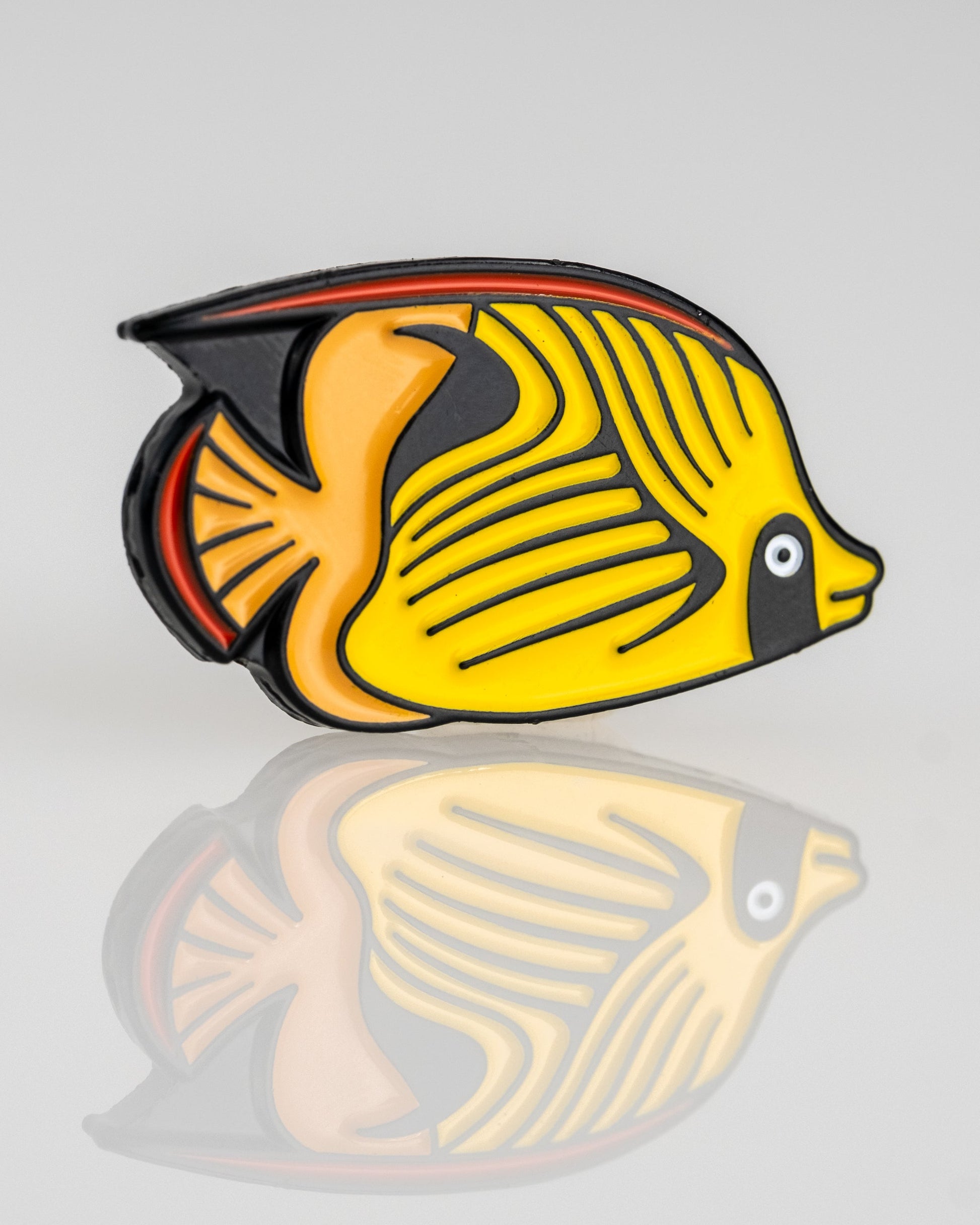 A vibrant Angel Fish with yellow, black, and orange markings appears on a light gray background with a polished reflection—featured in the Margaritaville - Angel Fish Ball Marker by Pins and Aces.