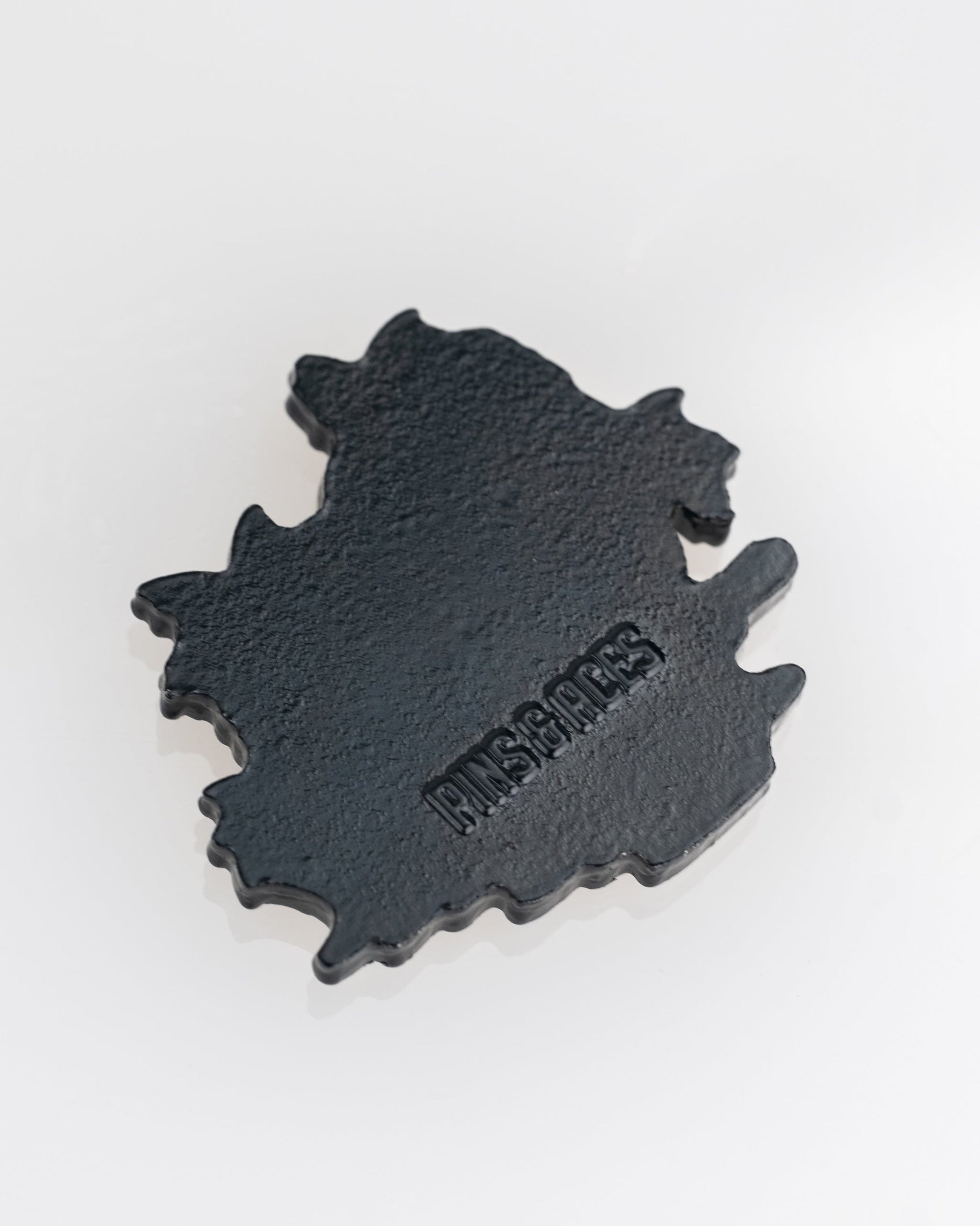 A black, irregularly shaped Margaritaville - Sleeping Parrot Ball Marker by Pins and Aces rests on a white surface, showcasing the brand's signature style.