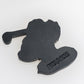 A black, flat, irregularly-shaped Margaritaville - Golfing Parrot Ball Marker by Pins and Aces with embossed PNGS.PGS text on one side—ideal for adding a unique flair to your golf ball marker collection.