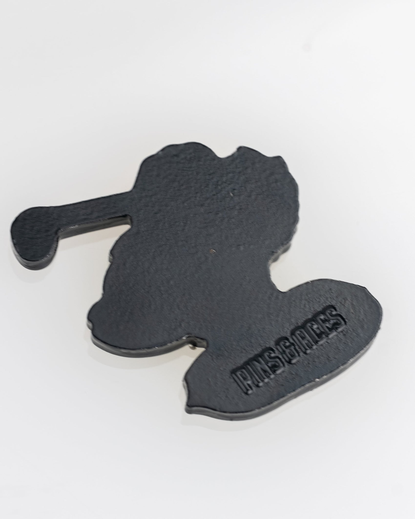 A black, flat, irregularly-shaped Margaritaville - Golfing Parrot Ball Marker by Pins and Aces with embossed PNGS.PGS text on one side—ideal for adding a unique flair to your golf ball marker collection.