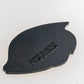 A black, leaf-shaped Margaritaville - Angel Fish Ball Marker by Pins and Aces, featuring a rough texture and embossed branding, is shown on a light, reflective background.
