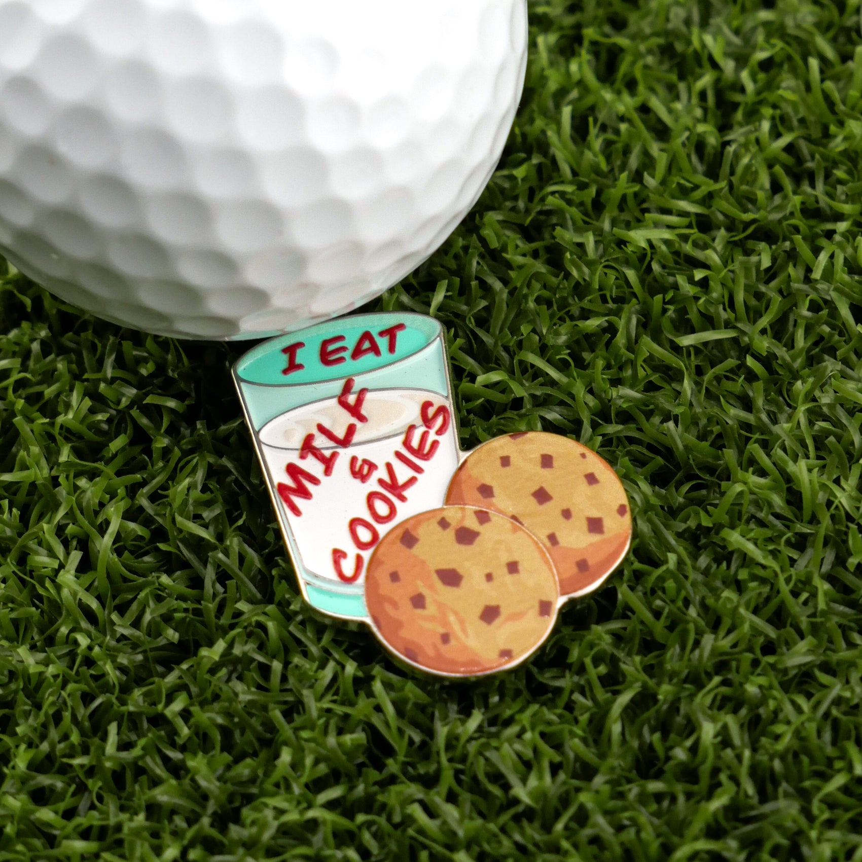The Logie Joe's Golf "Milf & Cookies" golf ball marker features a milk glass-shaped pin labeled “I EAT MILK & COOKIES,” two chocolate chip cookies, and a premium golf ball, making it a fun addition to any collection.